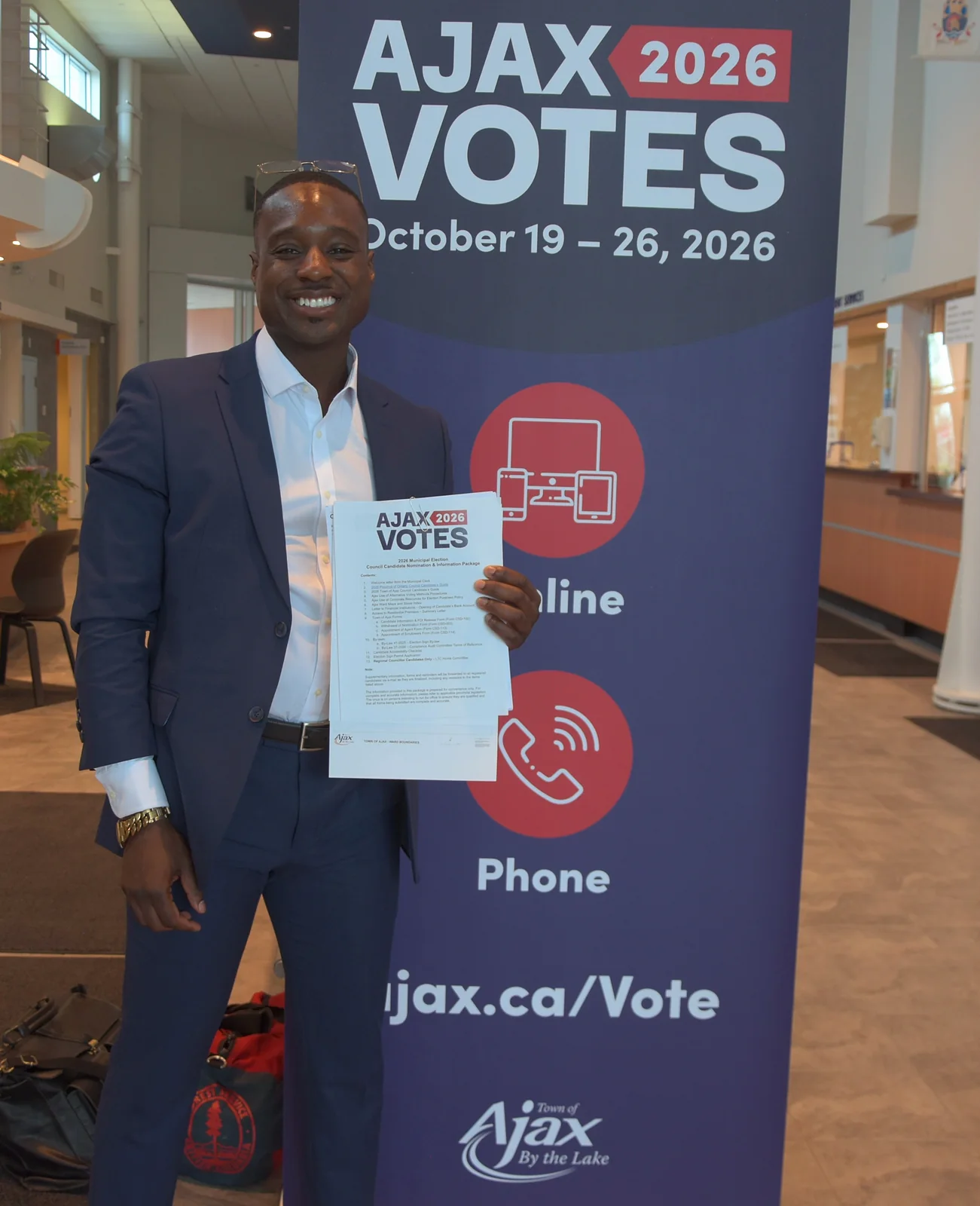 Jay Hayles holding voter information beside the Town of Ajax 'Ajax Votes 2026' banner